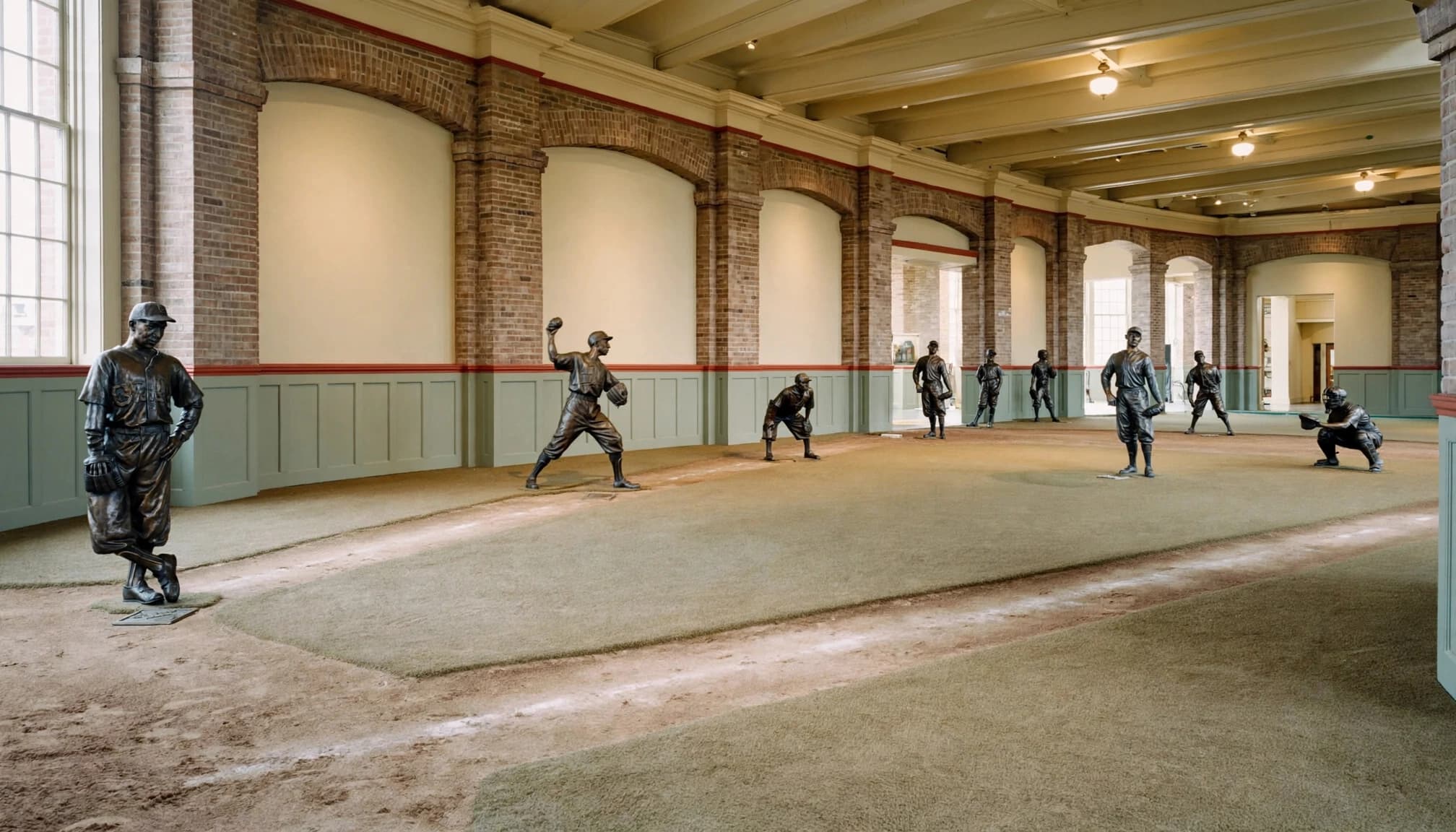 Bronze baseball players stand on a small indoor diamond in a warm-toned gallery.